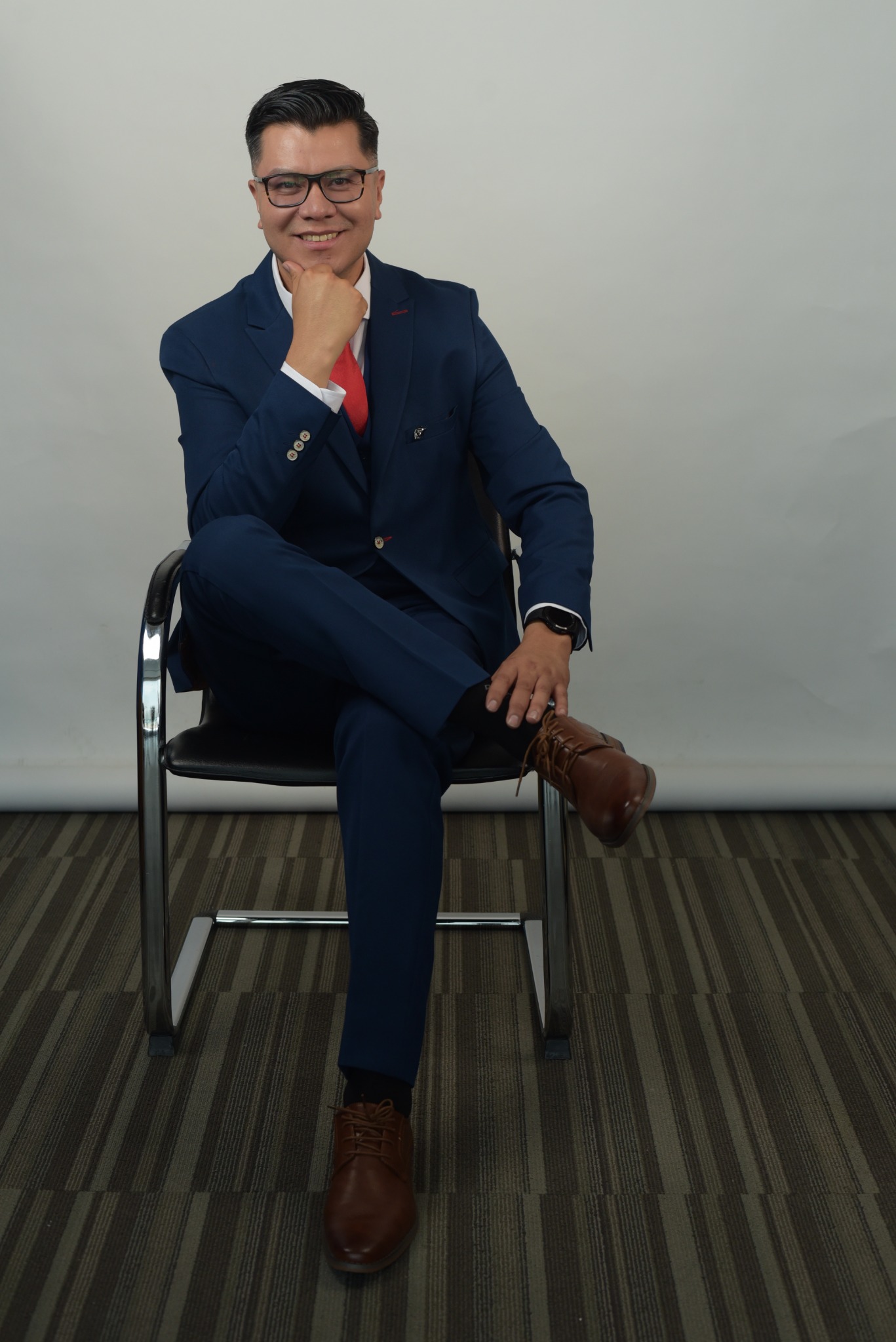 Alain Hernández sentado, con traje azul, en retrato profesional